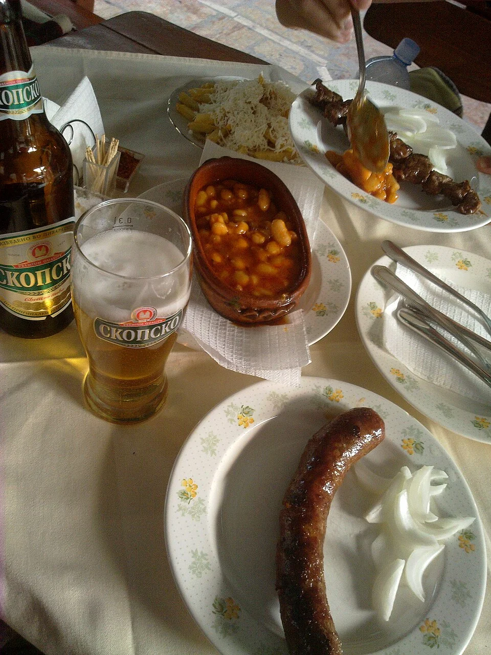 Tavče gravče örneğinin de bulunduğu yemek masası, Haziran 2011; yanında et ve içecek görülür. Belirli Üsküp restoranı veya etsiz menü olarak sunulmaz.
