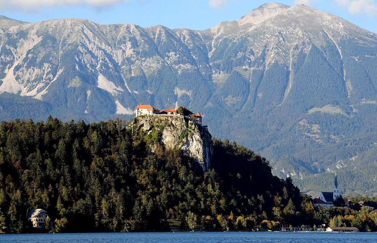 Bled Castle on the rocky height above the lake, with mountain scenery; September 2014.