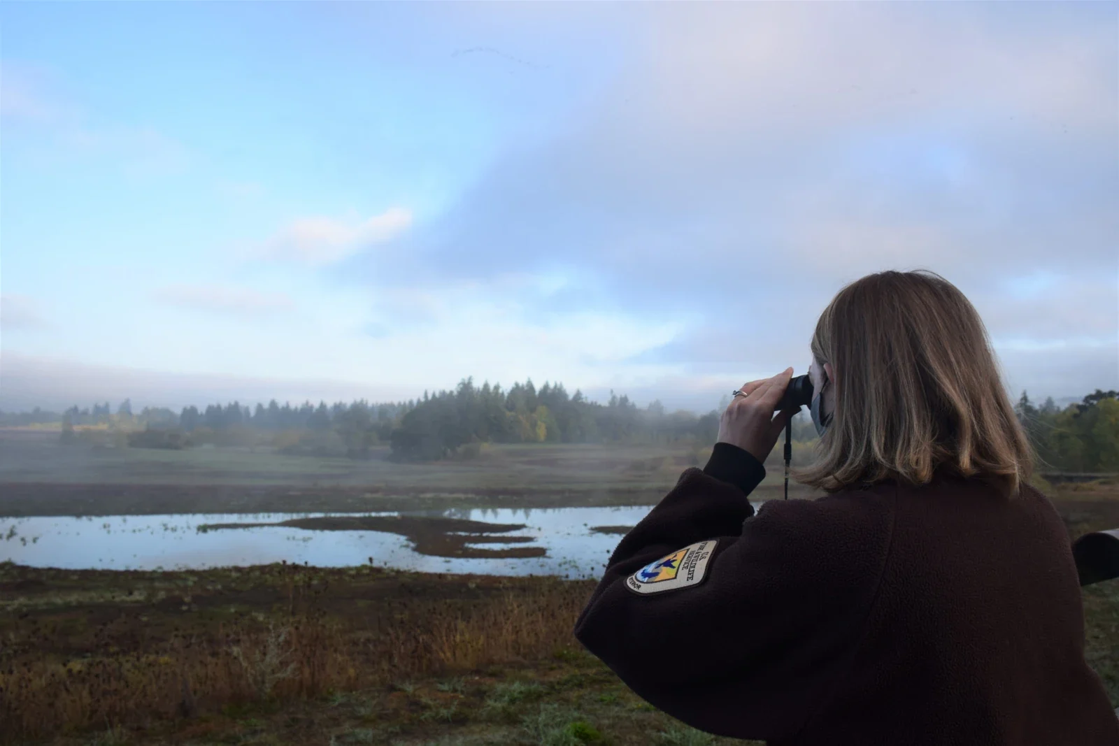 Staff member observing through binoculars at Tualatin River refuge in Sherwood, archive