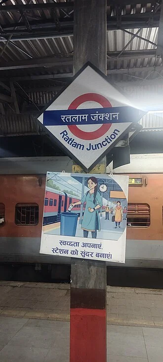 Ratlam Junction istasyon levhası, peron çatısı ve arkasındaki tren
