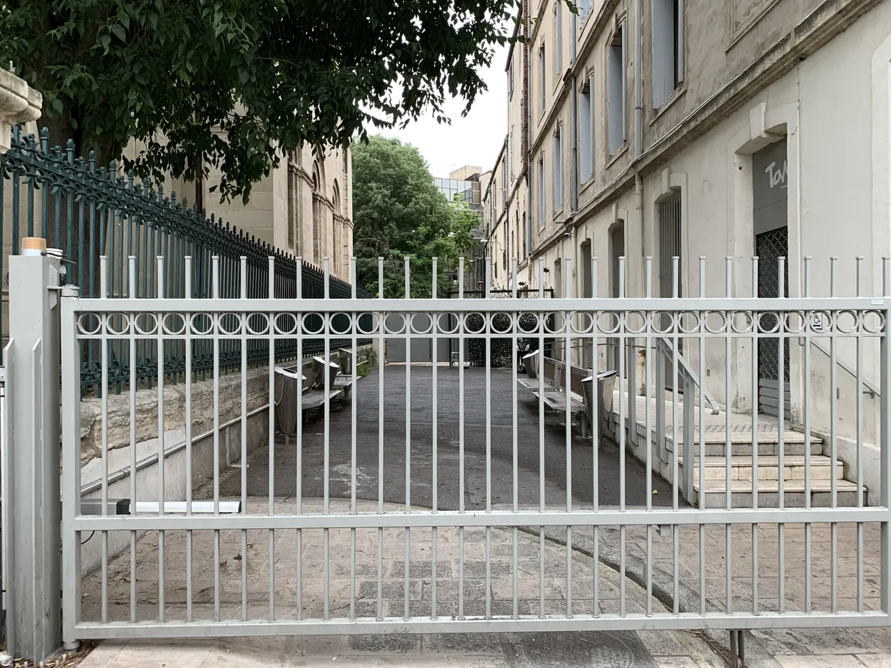 Closed iron gate at the entrance to Impasse du Temple and buildings behind it, Montpellier, June 2019