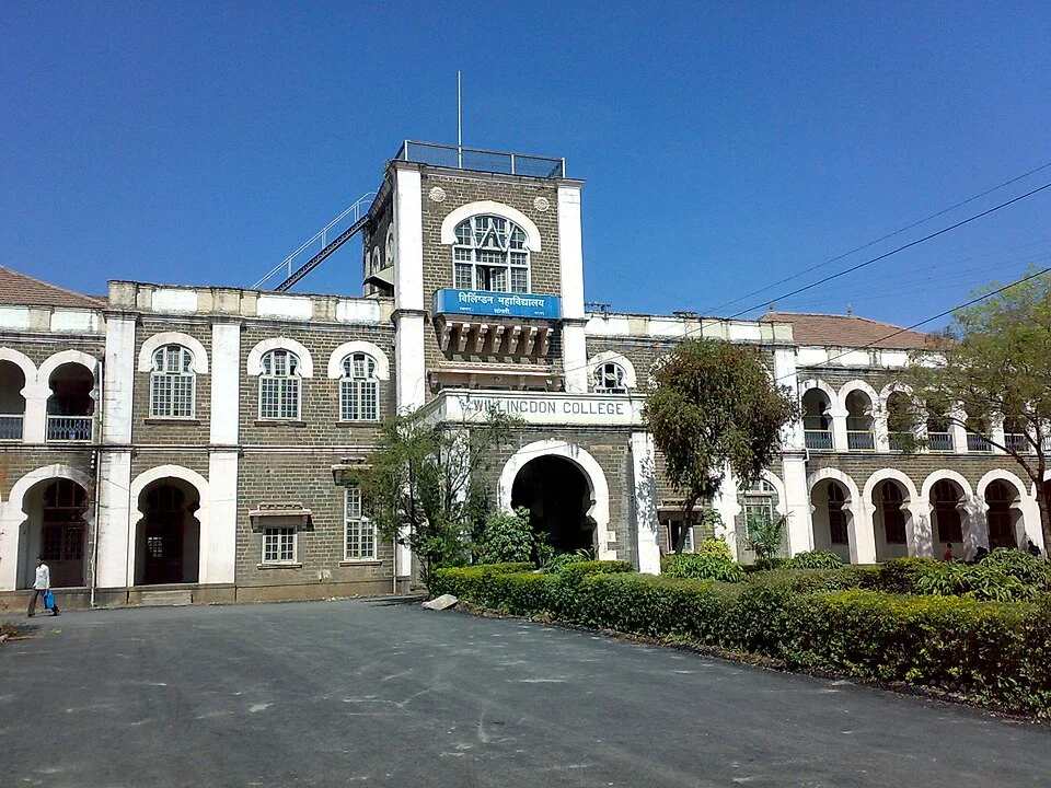 Stone facade, white arches and planted foreground of Willingdon College in Sangli