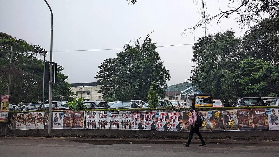 Tree-lined Kannur urban road with vehicles and a roadside wall