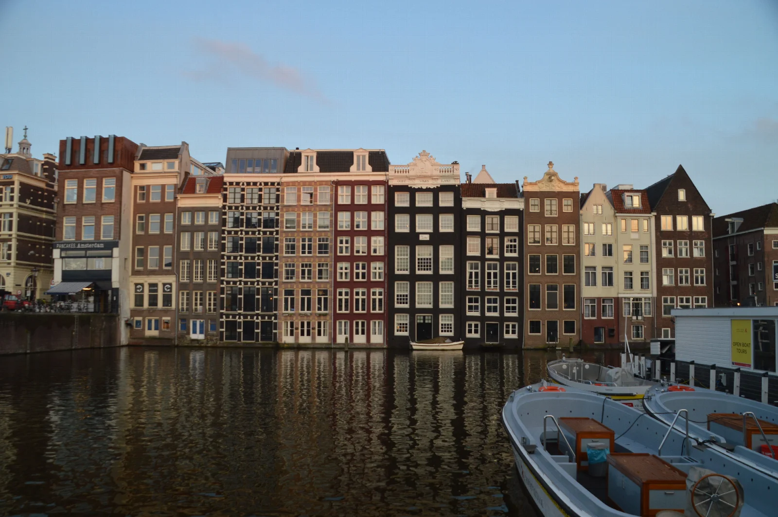 Amsterdam’da farklı çatılara sahip dar kanal evleri, suya düşen yansımaları ve kıyıya bağlı tekneler