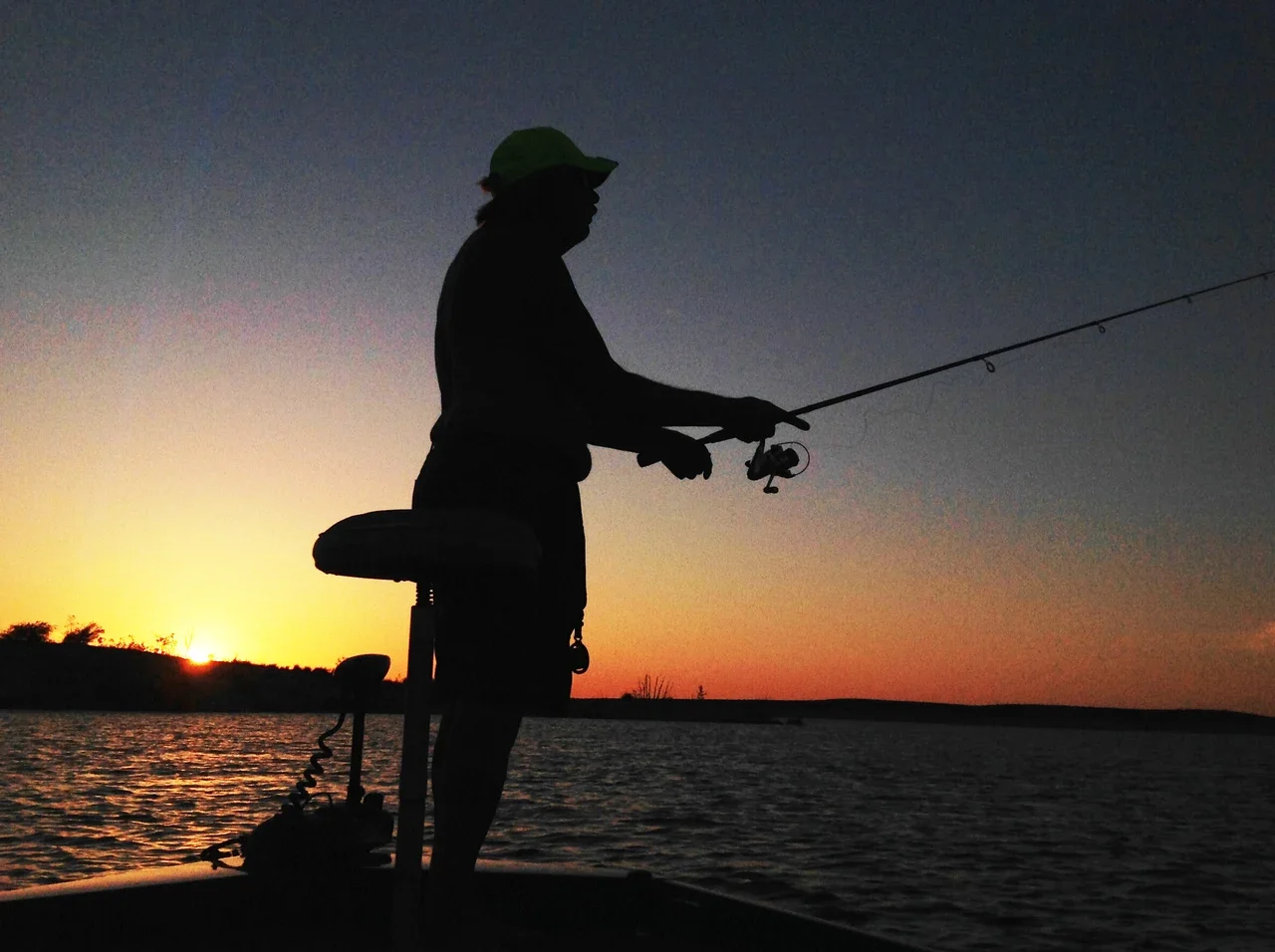 Angler silhouette holding a fishing rod at sunset on Amistad