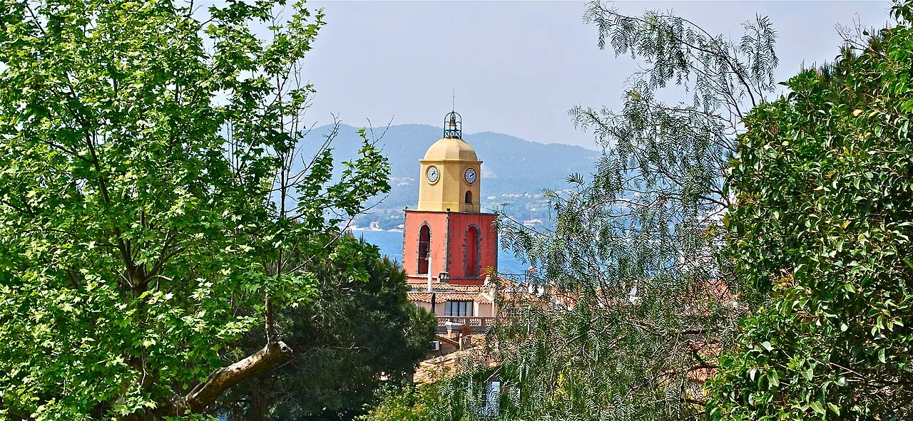 Saint-Tropez Notre-Dame de l'Assomption çan kulesi, ağaçlar ve körfez; Nisan 2011.