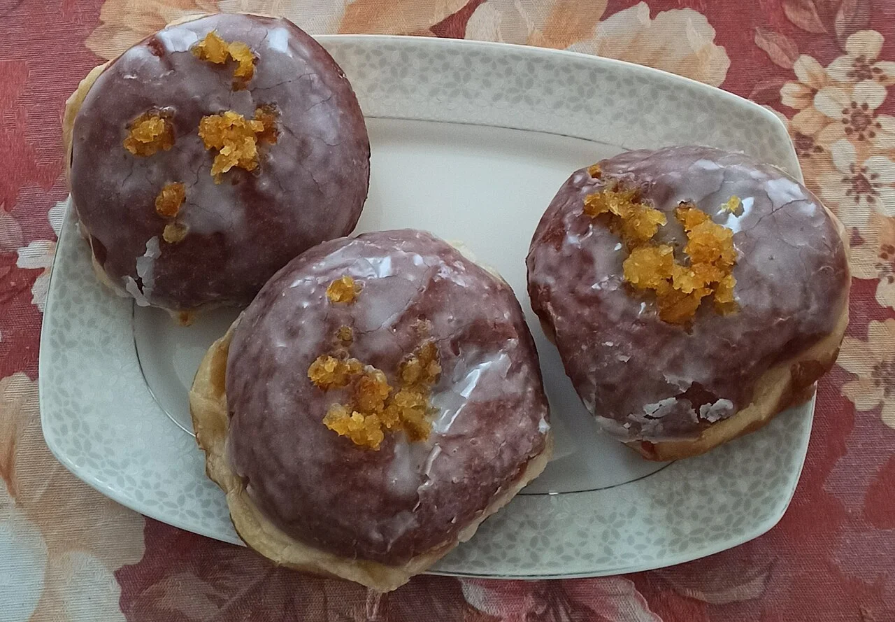 Three illustrative pączki pastries; February 2026, location unconfirmed, not an endorsement of a Kraków pastry shop.