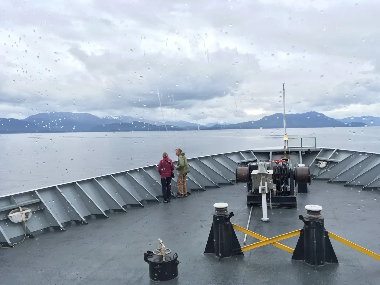 Ferry bow deck and passengers seen through a rain-marked window