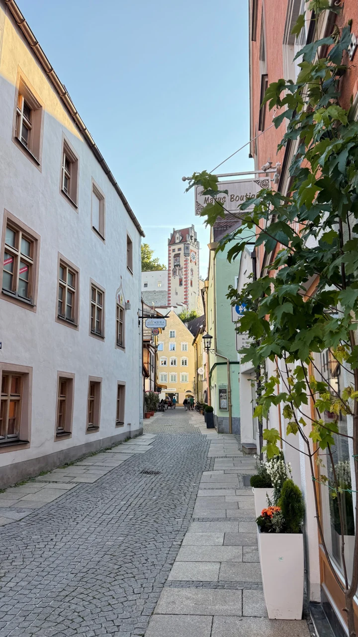Füssen’de taş döşeli dar sokak ve uzakta saatli kilise kulesi