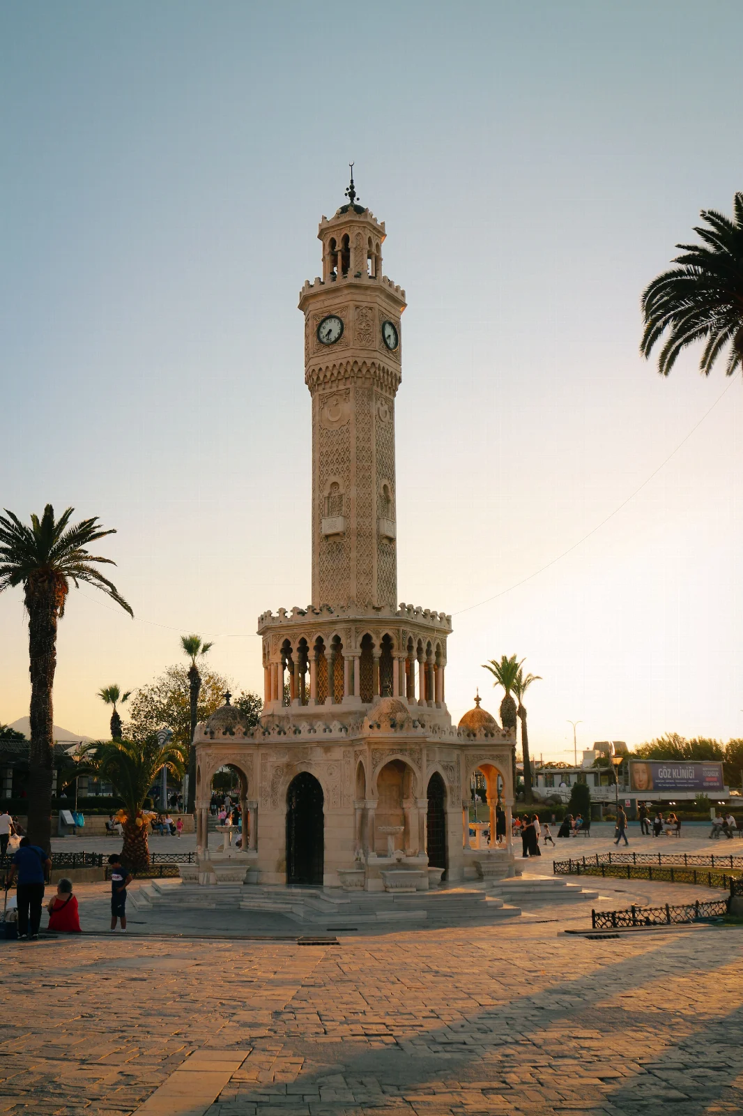 İzmir Konak Meydanı’ndaki Saat Kulesi, palmiye ağaçları ve akşam ışığında meydanda yürüyen insanlar