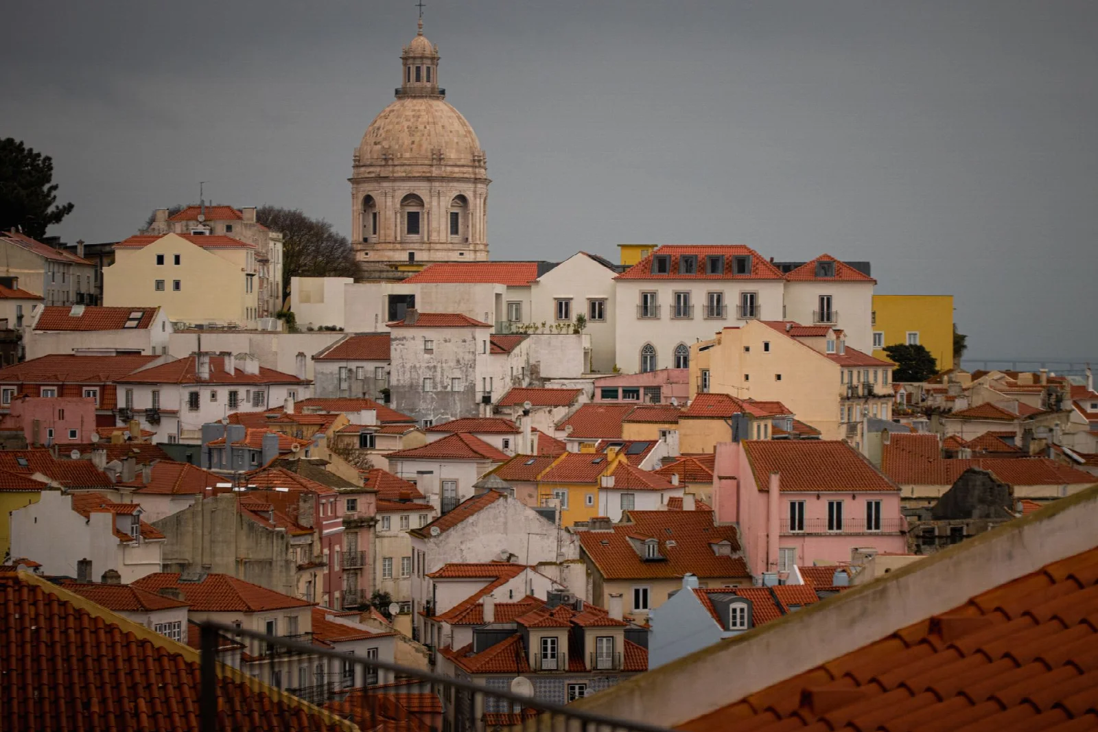 A dome rising above terracotta rooftops and colorful historic buildings in Lisbon