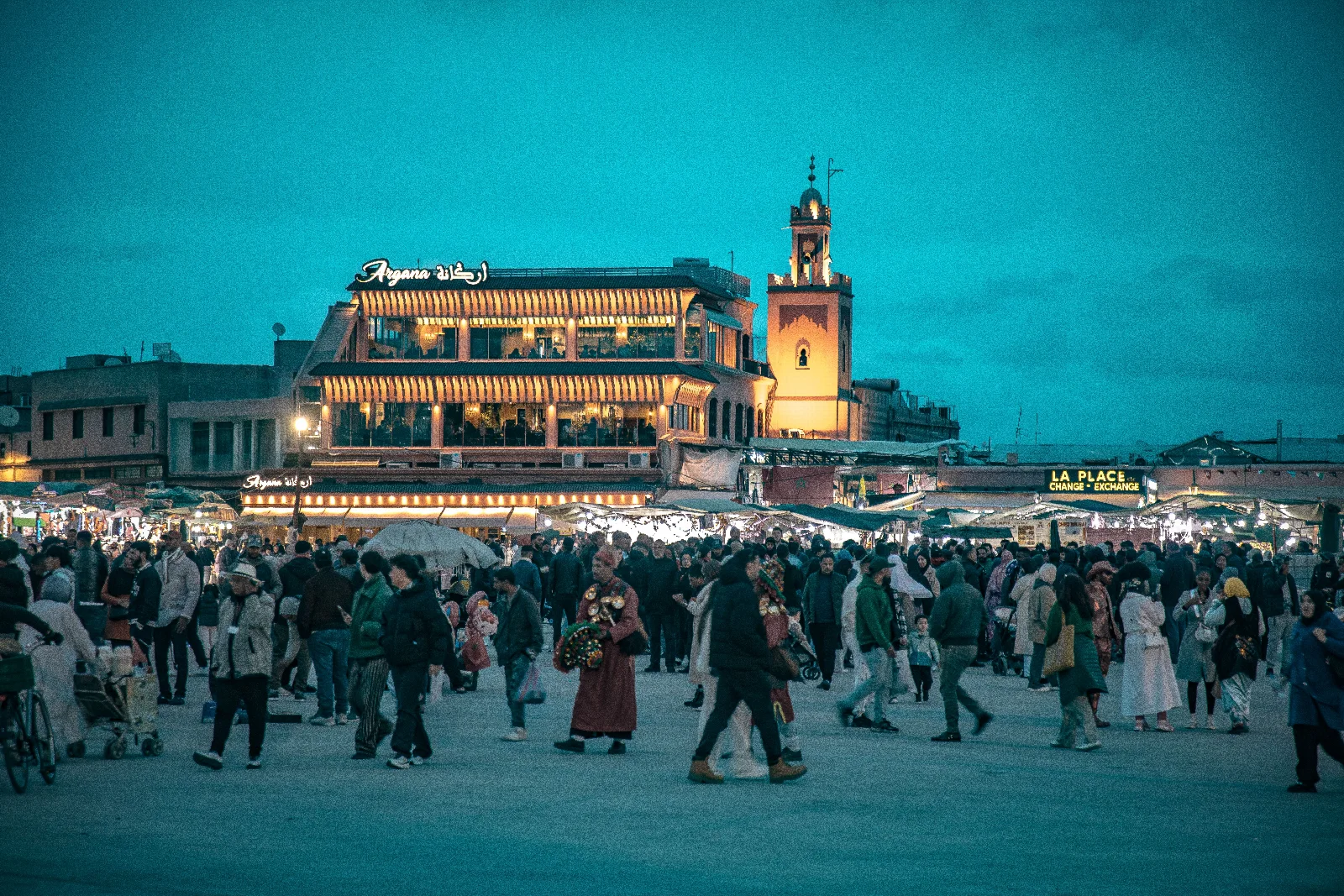 Marakeş’te Jemaa el-Fna Meydanı’nda akşam kalabalığı, ışıklı teraslar ve mavi gökyüzü