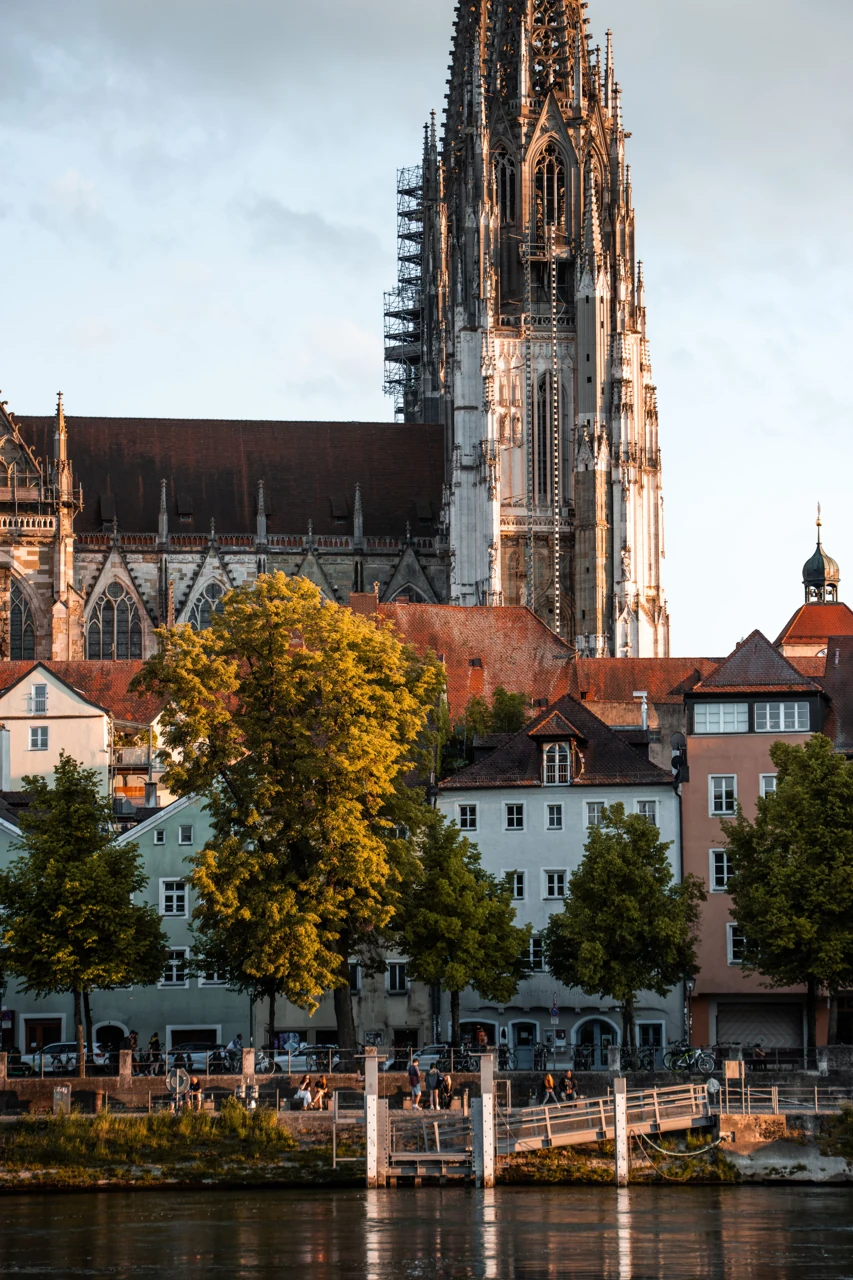 Colourful Danube-side houses with part of a cathedral tower and exterior wall in view.