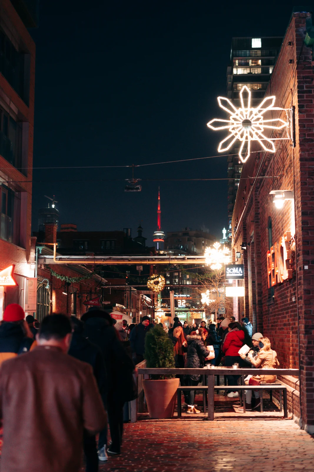 A night-time street between brick buildings in Toronto’s Distillery District, lit by seasonal decorations